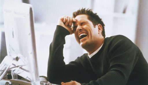 man_in_office_sitting_at_computer_hand_on_forehead_laughing_pbc13045