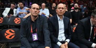 Οι Παναγιώτης και Γιώργος Αγγελόπουλος καθισμένοι δίπλα στο παρκέ σε αγώνα μπάσκετ